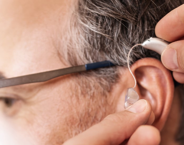 Mann beim Anlegen von Hinter-dem-Ohr-Hörgeräten